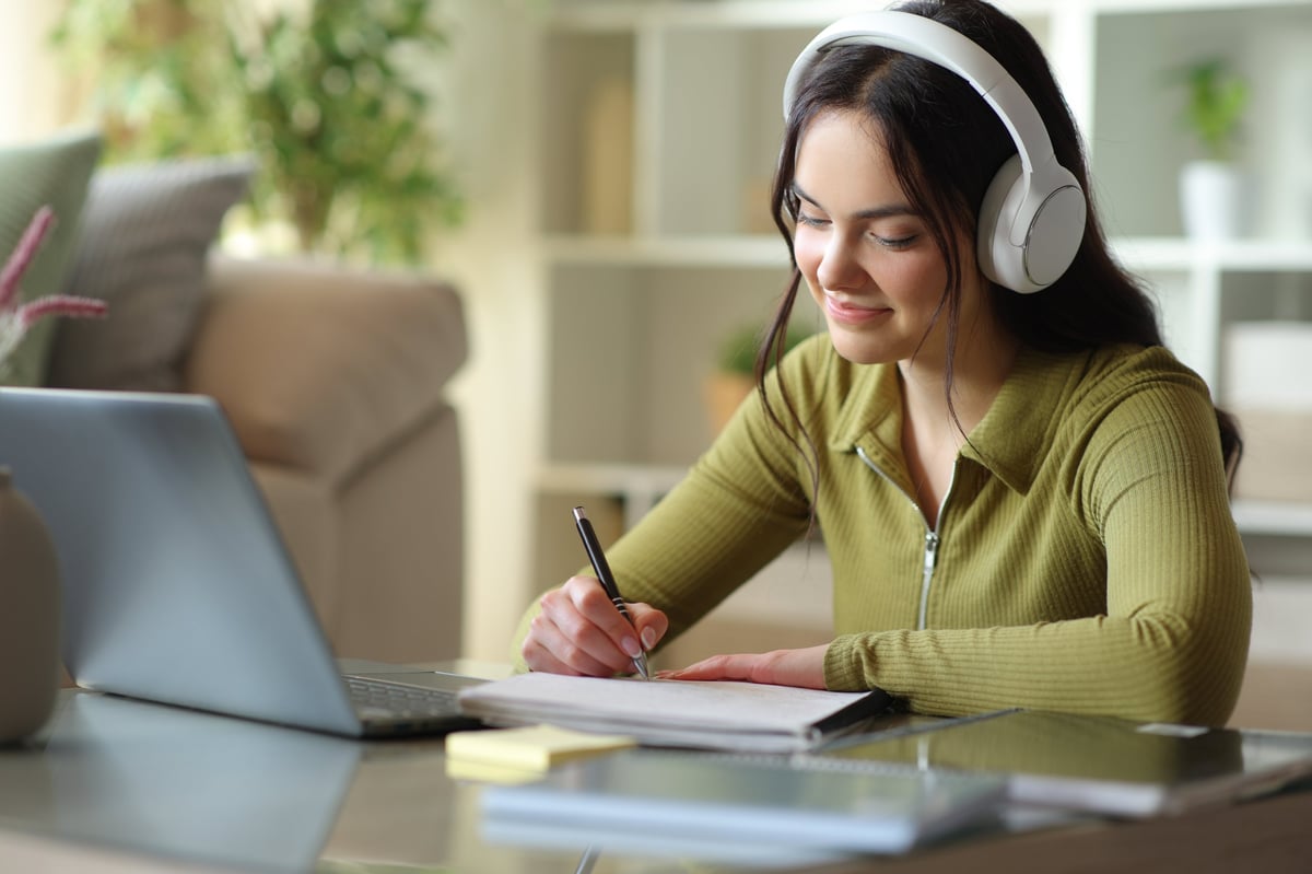 Estudiante con audífonos tomando apuntes mientras estudia inglés online en casa